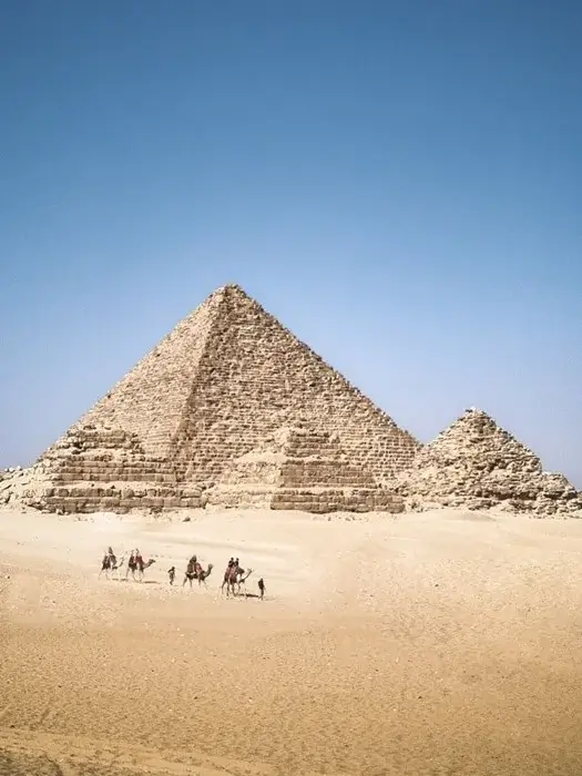 Camel caravan crossing the sand before the Pyramid of Menkaure in Giza, a classic sight on a luxury trip to Egypt