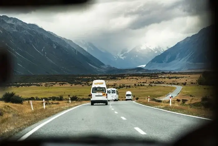 White campervans on an alpine highway toward snow-capped mountains, a typical road trip scene for anyone comparing New Zealand campervan pricing
