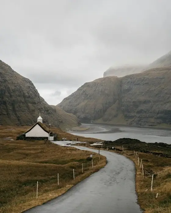 Winding road leading to a white turf-roofed church and tidal lagoon in Saksun, Faroe Islands, an inspiring stop when you plan a Nordic trip