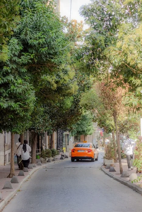 Orange taxi driving down a quiet tree-lined street, a reminder to use ride-hailing apps or taxis when getting around on your trip