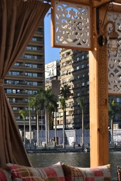 Traditional Egyptian-style boat lounge with a hanging lantern overlooking high-rise buildings across the river