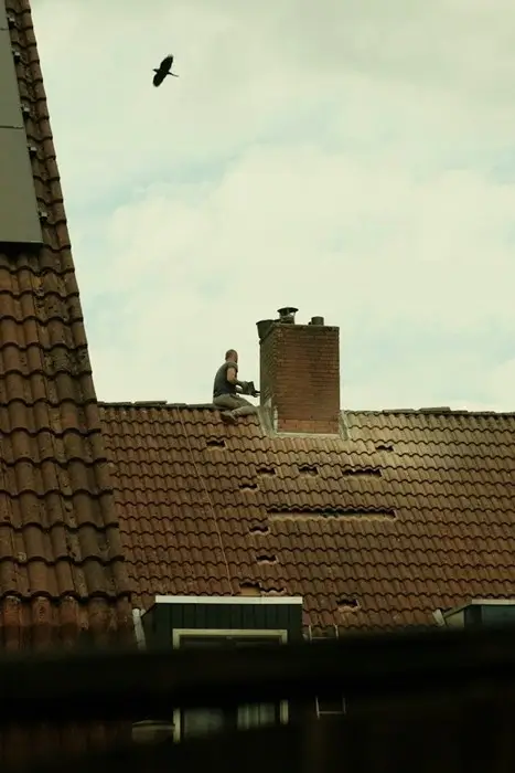 Roofer working beside a brick chimney on a tile roof with gaps where tiles are missing or out of place