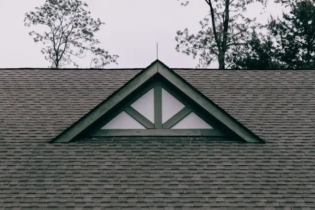 Asphalt shingle roof with a triangular gable dormer framed in dark trim, under an overcast sky