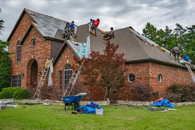 Roofing crew replacing shingles on a two-story brick home, the kind of full roof job a roofing company in Austin, TX takes on
