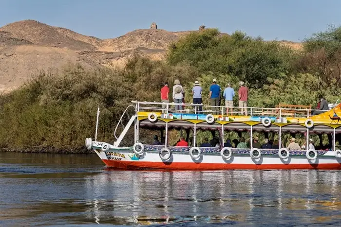 Small group of tourists on the upper deck of a painted river boat sailing beneath sandy cliffs