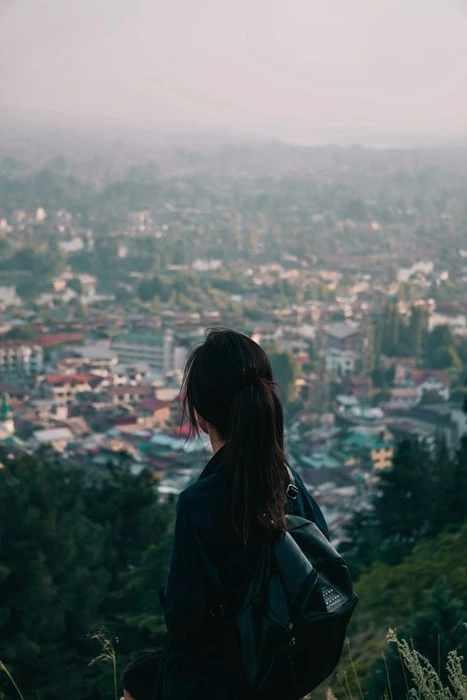 Woman with a ponytail and black backpack overlooking a hazy city from a hillside during solo travel after breakup
