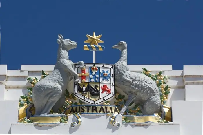 The Australian coat of arms with a kangaroo and emu on the white facade of Old Parliament House, a proud symbol for visitors exploring Canberra’s past