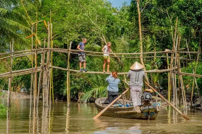 Rowing boat gliding under a bamboo bridge surrounded by palm trees in the Mekong Delta, a peaceful place to visit in Vietnam