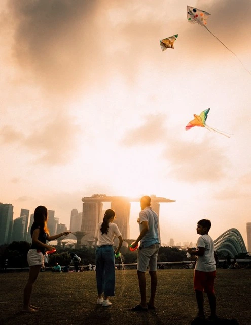 A family flies colorful kites on the lawn at Marina Barrage at sunset, with Marina Bay Sands and the Gardens by the Bay domes in the distance, a relaxed way to end a day in Singapore with kids