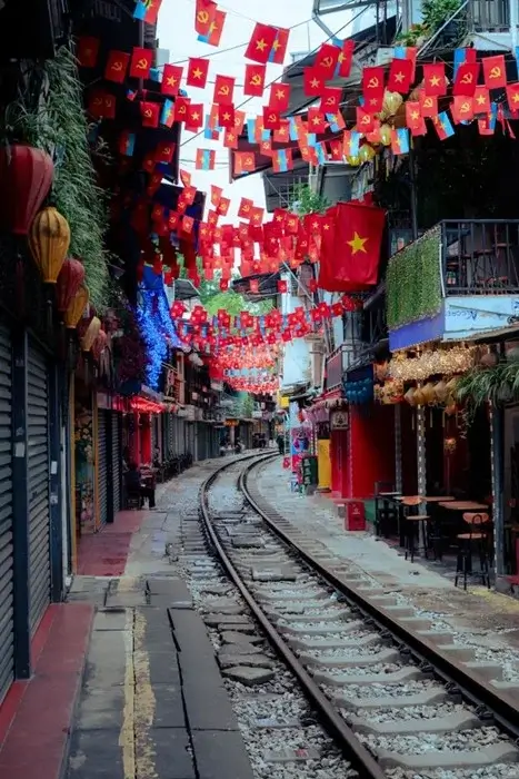 Narrow railway running between colorful shophouses and hanging Vietnamese flags on Train Street in Hanoi, Vietnam