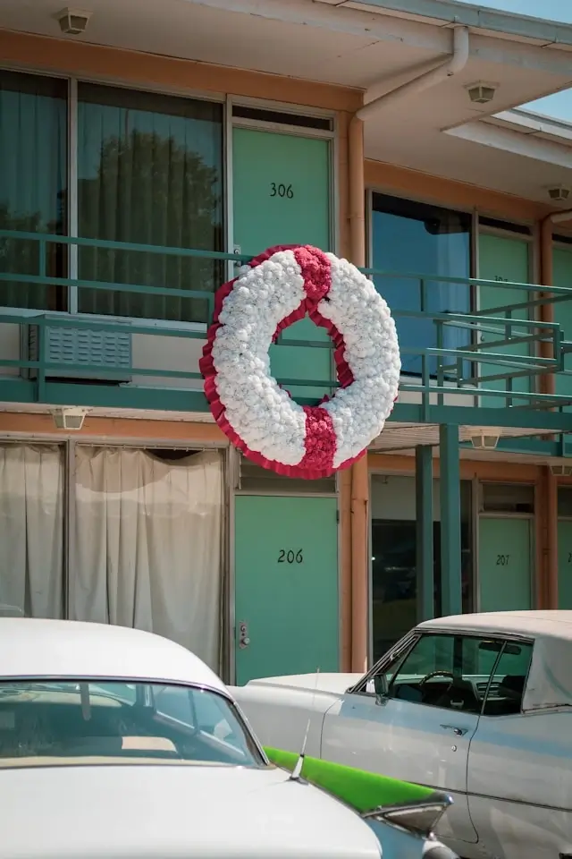 Exterior of the Lorraine Motel in Memphis, TN, showing room 306 with a large white and red wreath on the balcony railing, and vintage cars parked below.