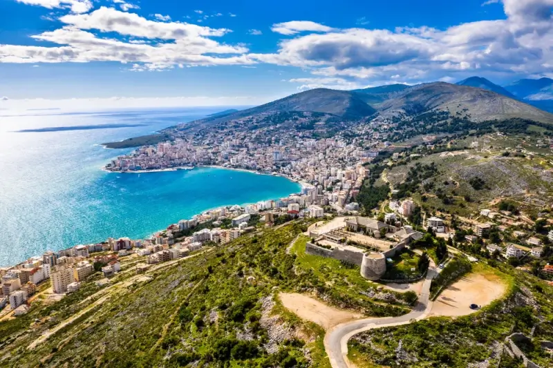 Aerial view of Albanian Riviera coastline with Saranda Bay, turquoise waters, and ancient hilltop fortress overlooking Mediterranean Sea