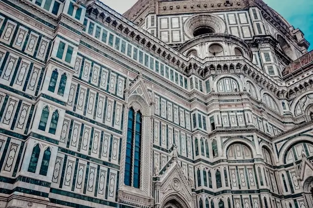 Close-up architectural detail of Florence Cathedral (Duomo) showing intricate geometric marble patterns in white, green, and pink with Gothic Revival decorative elements