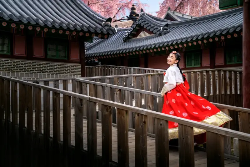 Woman wearing traditional Korean hanbok dress at historic Korean palace with traditional architecture, showcasing Korean culture that travelers can experience while practicing basic Korean language skills