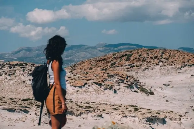 Woman with dark backpack exploring rocky Mediterranean landscape - essential preppy travel gear for hiking adventures