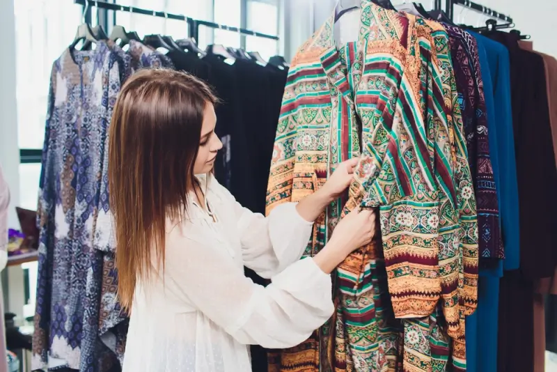 Woman selecting colorful patterned abaya from clothing rack while shopping for modest fashion in boutique