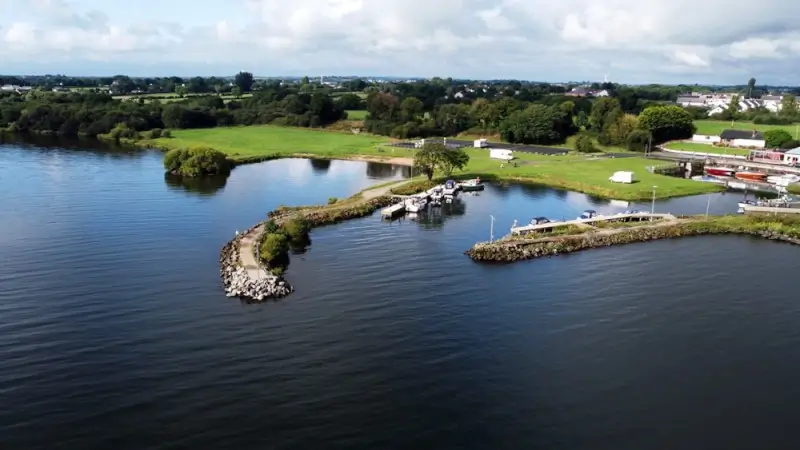 Aerial view of Irish lough with marina, boats, and green countryside stretching to distant hill