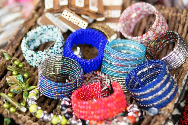Colorful handmade beaded bracelets and jewelry displayed in wicker basket featuring blue, pink, coral, green and white beaded accessories