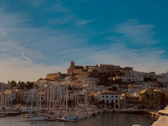 Ibiza Town harbor at sunset with white Mediterranean buildings, historic Dalt Vila fortress, and luxury yachts in marina - iconic Ibiza destination compared to Caribbean islands