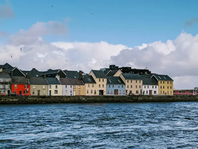 Colorful row houses along Irish harbor waterfront with seagulls flying over blue water