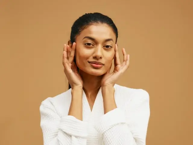 Woman with glowing skin gently cupping face in white bathrobe demonstrating healthy skin tips routine