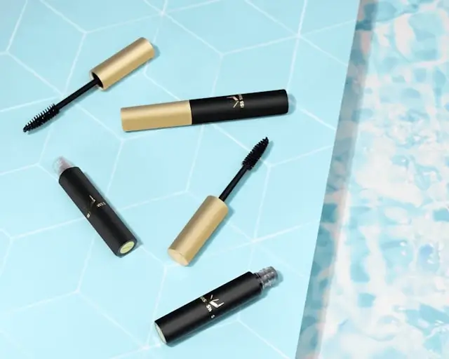 Collection of black and gold mascara tubes for lash growth arranged on blue tile surface