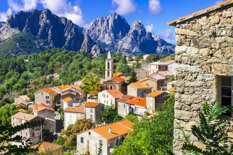 Traditional Corsican mountain village with stone houses, red tile roofs, and church bell tower against dramatic granite peaks