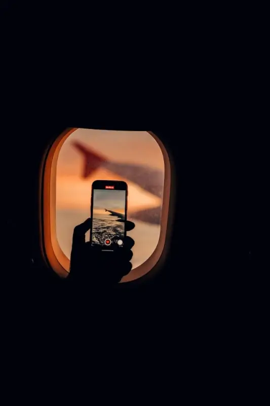 Solo traveler capturing sunset photo through airplane window - creative digital activity ideas for documenting travel experiences