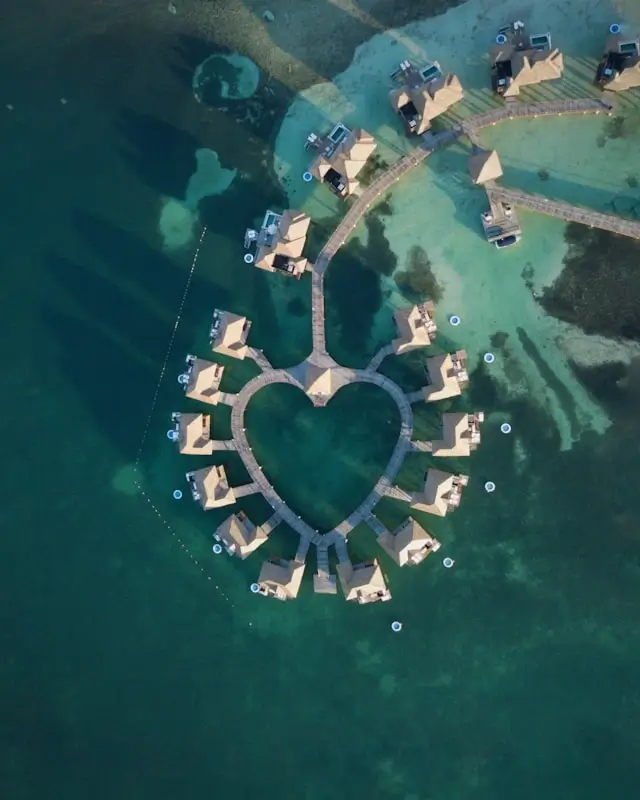 Aerial view of luxury overwater bungalows arranged in heart shape over turquoise Caribbean lagoon - romantic Caribbean resort accommodation versus Ibiza hotel options