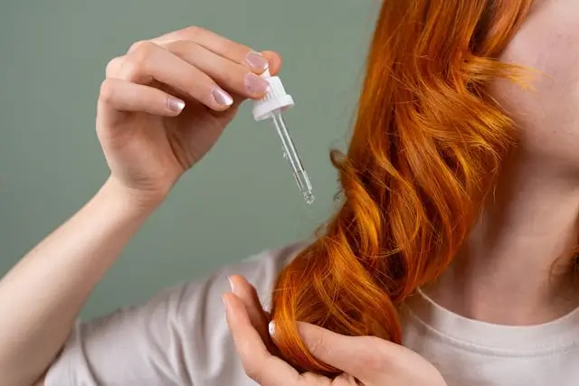 Woman applying rosemary oil with dropper to vibrant red hair, demonstrating travel-friendly hair care benefits for healthy locks on the go