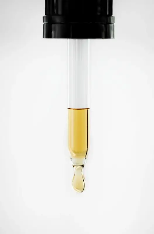 Golden rosemary oil drop forming at dropper tip, showing pure concentrate and precise application benefits for travelers' skincare routines
