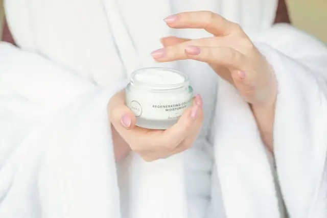 Hands holding regenerating moisturizer jar in white robe showing daily healthy skin tips routine