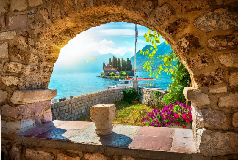 Stone archway in Montenegro's Bay of Kotor with view of fjord-like inlet, historic church on island, and mountain backdrop