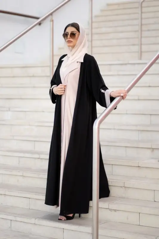 Woman in black abaya with pink trim and cream hijab demonstrating elegant modest fashion on steps