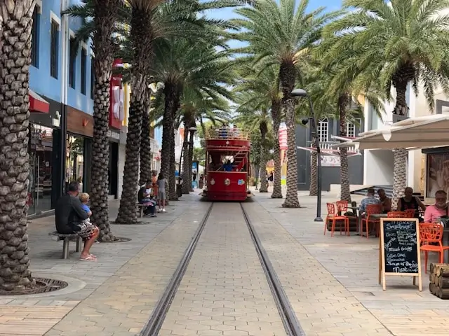 Red trolley on palm-lined Caribbean promenade with outdoor cafes and colonial architecture - Caribbean island town atmosphere versus Ibiza urban experience
