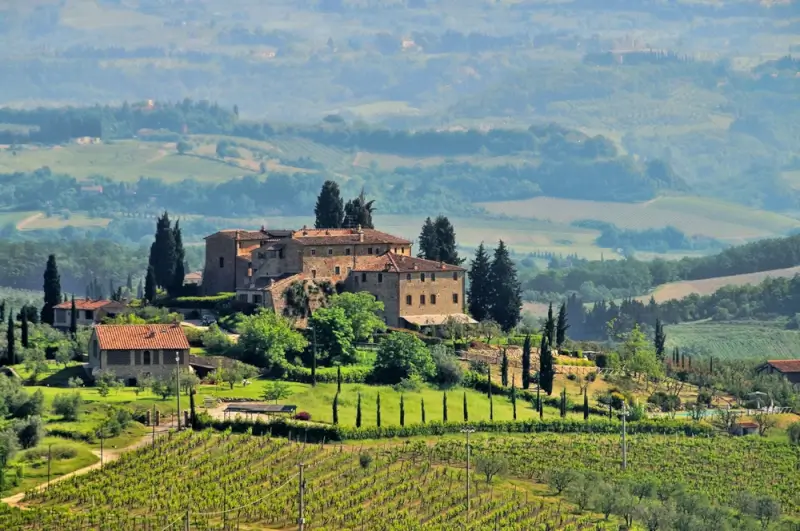 Historic Tuscan villa and estate surrounded by tall cypress trees overlooking vineyards and rolling hills in the misty countryside
