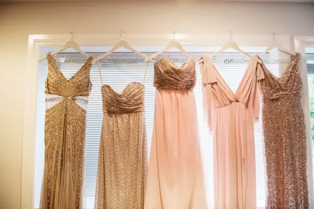 Five elegant wedding guest dresses hanging on display - gold sequined and peach formal gowns for special occasions