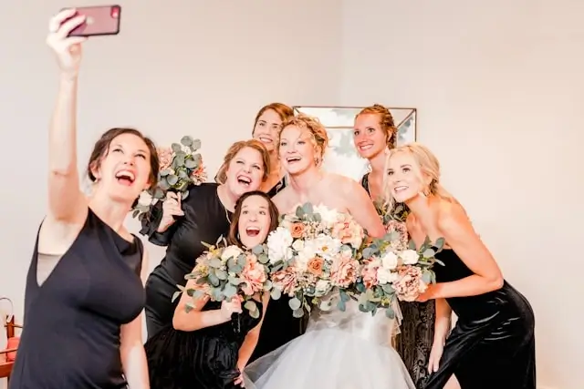 Bride and wedding guests in coordinated black dresses taking selfie, elegant dark formal wedding guest outfits