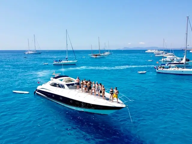 Luxury yacht party with crowds on deck in crystal blue Ibiza waters surrounded by sailboats - famous Ibiza boat party scene compared to Caribbean yacht charters