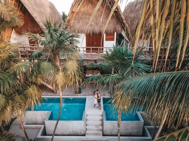 Couple enjoying romantic tropical resort accommodation with thatched roof villas and private swimming pool surrounded by palm trees