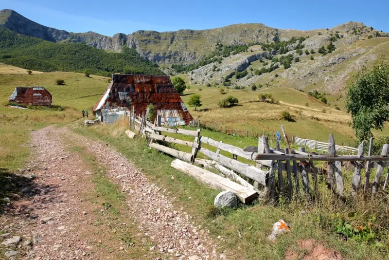 Traditional mountain shepherd huts with rustic wooden fencing set against dramatic limestone peaks in Bjelasnica mountain, representing authentic rural culture along hiking trails