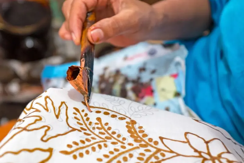 Traditional batik making class in Indonesia showing hands applying wax resist dyeing technique