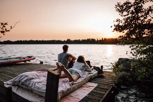 Romantic couple relaxing together on wooden dock by lake at sunset, enjoying peaceful moment during their travel adventure