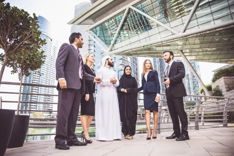 Diverse business professionals in formal attire meeting outside modern Dubai office building, representing international partnerships in UAE business setup