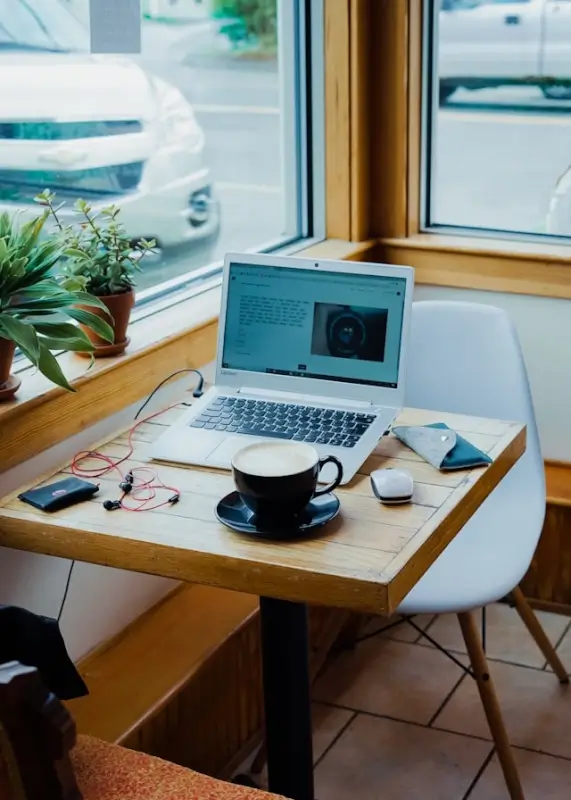 Freelancer workspace with laptop, coffee, and plants by window showing remote work setup in UK home office