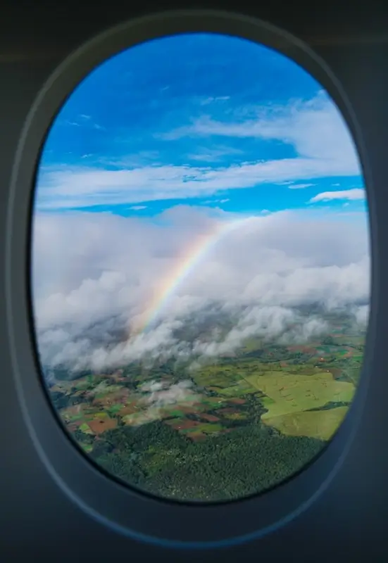 Airplane window view of rainbow over green landscape representing transformative travel learning experiences