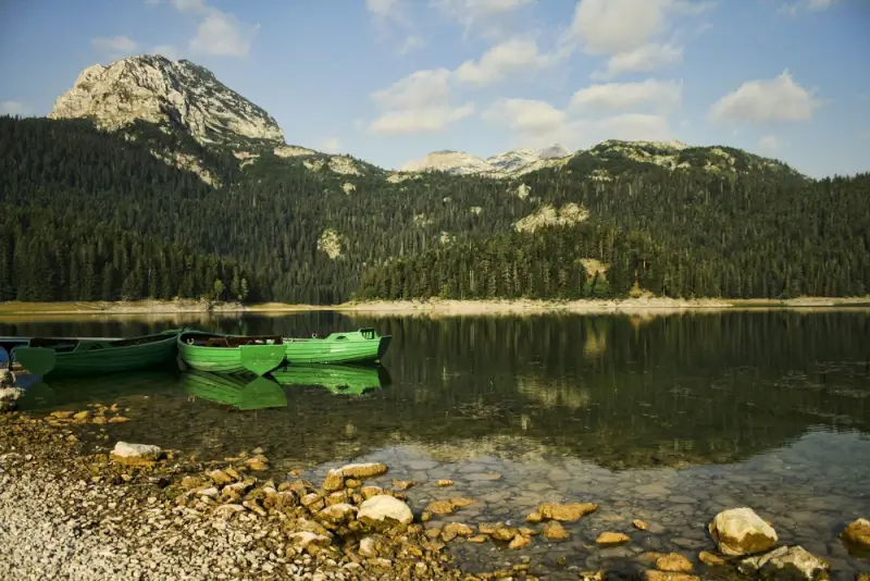 Green wooden boats on pristine mountain lake surrounded by forested peaks in Durmitor National Park, perfect for kayaking and water-based outdoor adventures