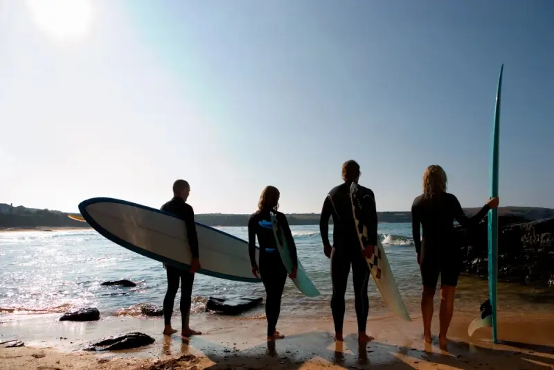 Group of surfers in wetsuits holding surfboards on beach during surfing retreat lesson