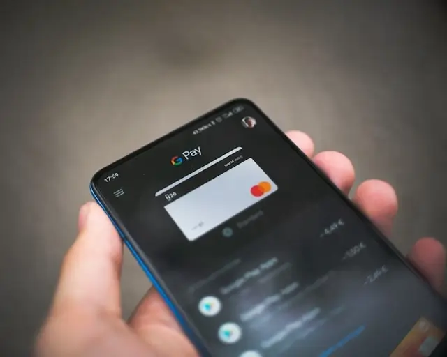Hand holding smartphone with Google Pay app showing digital payment card, representing mobile money management for digital nomads
