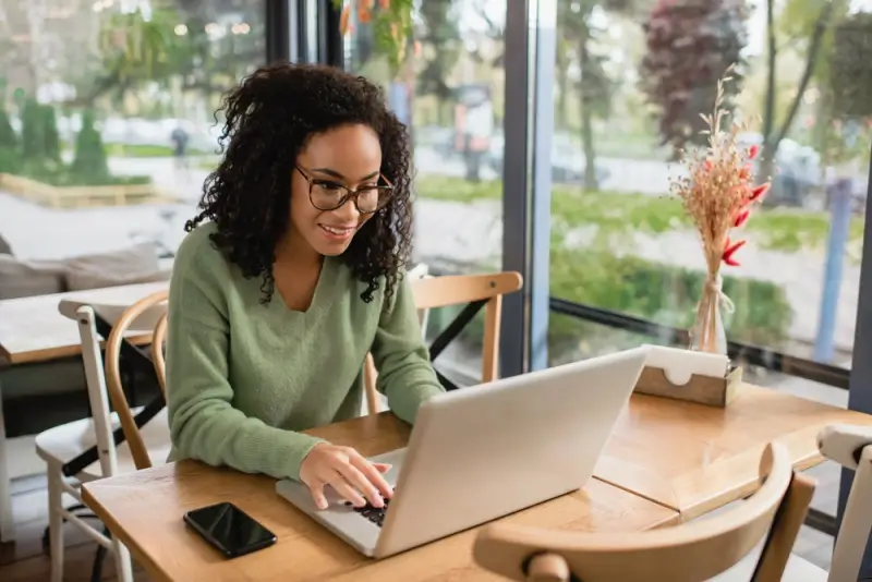 Smiling woman working on laptop in cafe, representing freelancers who work legally in UK with proper visa and registration